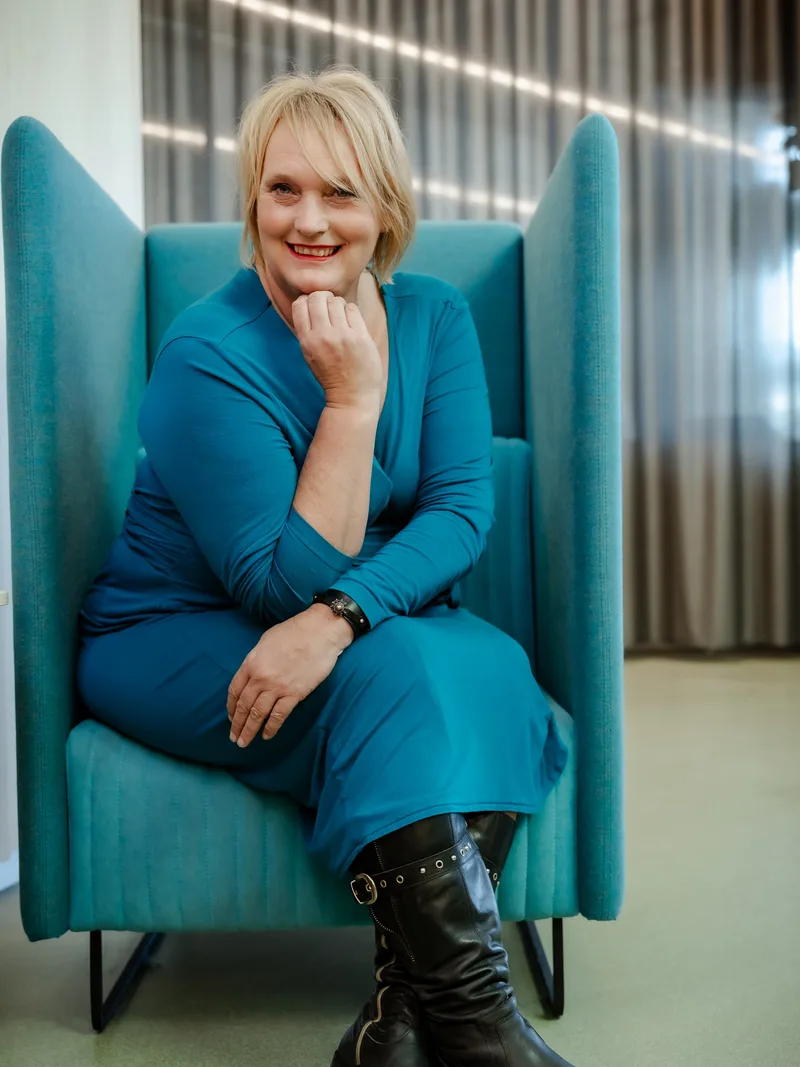 Anita Viergever, lachend in een hoge blauwe fauteuil